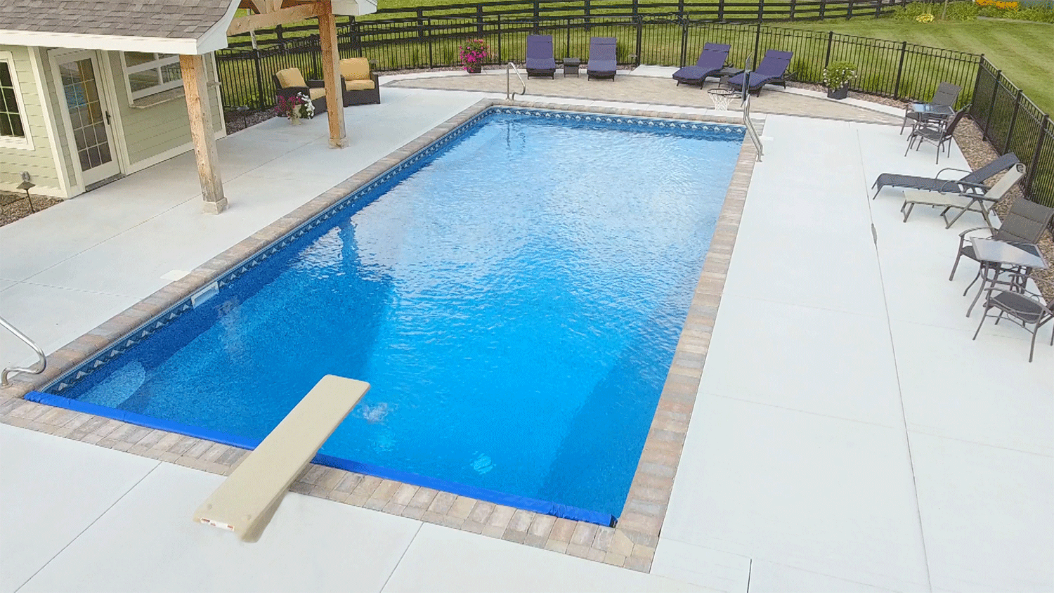 Rectangular inground vinyl liner pool with diving board and pool house.
