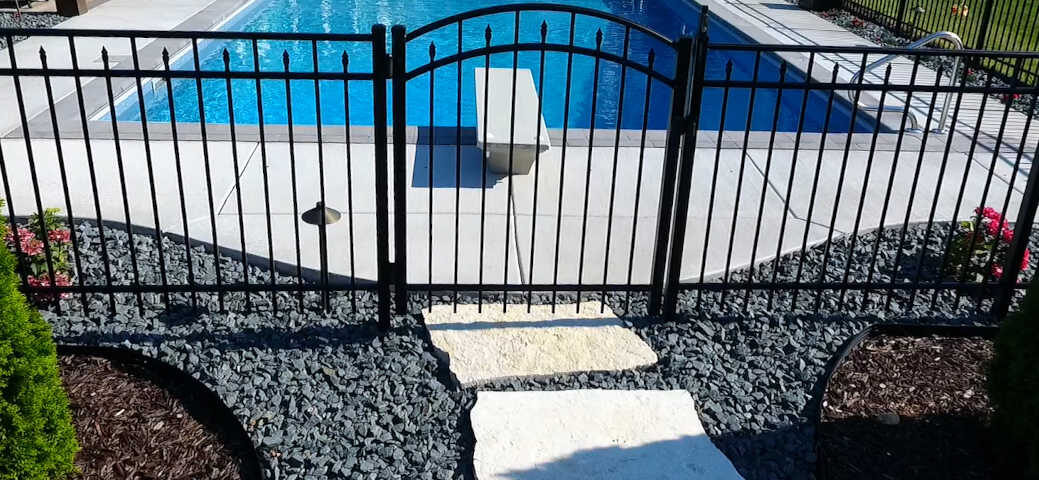 Black aluminum fence with a single arched gate surrounding a rectangular inground pool.