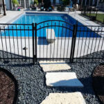 Black aluminum fence with a single arched gate surrounding a rectangular inground pool.